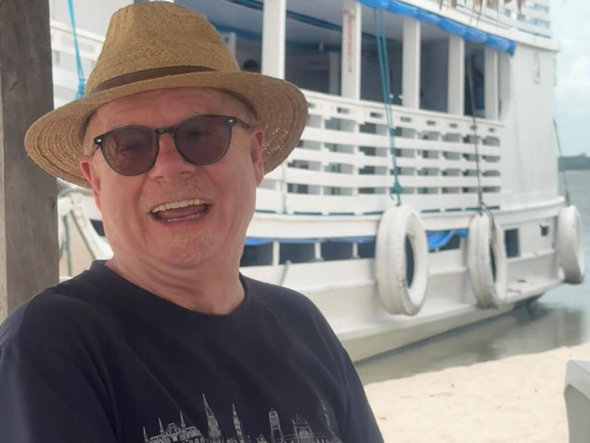 Paul sitzt mit Sonnenhut vor einem Boot im Amazonasgebiet