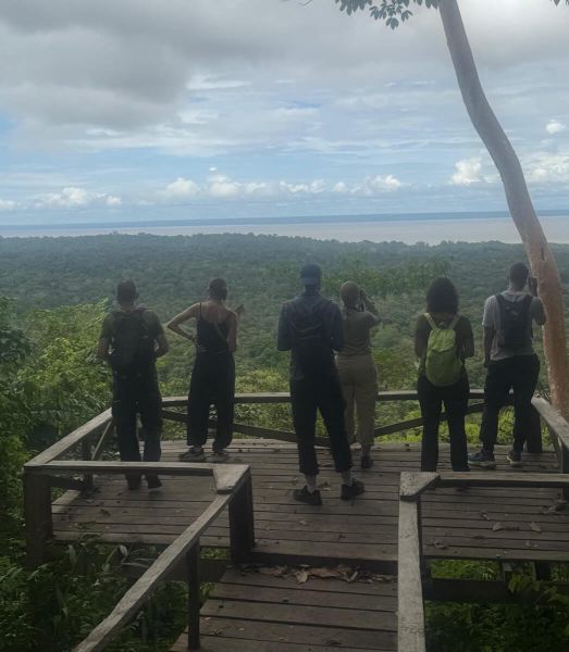 Gruppe blickt von einer Holzplattform über den Amazonas-Regenwald und einen breiten Fluss