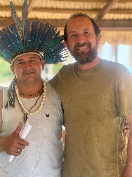 Marcio Halla steht gemeinsam mit einem Cacique mit traditionellem Kopfschmuck in einer offenen Hütte im Amazonasgebiet