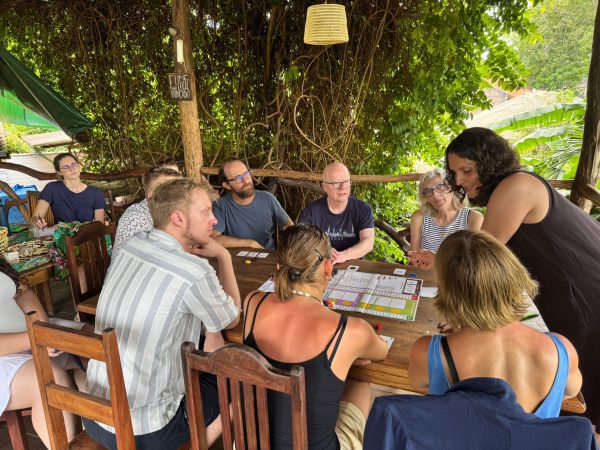 Mehrere Personen sitzen an einem Holztisch und nehmen an einem Workshop mit Spielmaterial teil