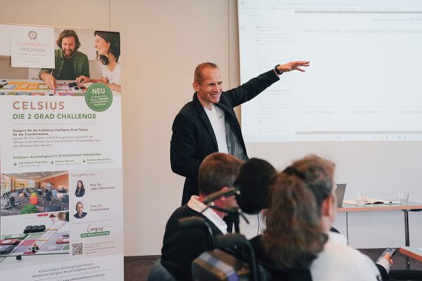 Ein Referent erklärt in einem Workshop eine Frage zum CO2-Fußabdruck, daneben steht ein Celsius-Roll-up