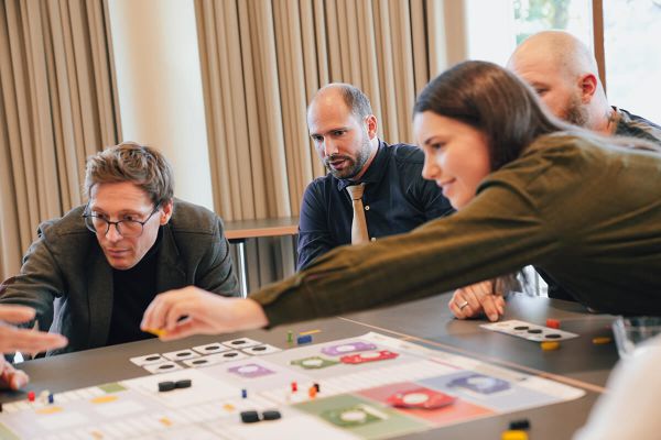 Mehrere Teilnehmende sitzen an einem Tisch und greifen nach Spielsteinen auf dem Spielfeld von Celsius