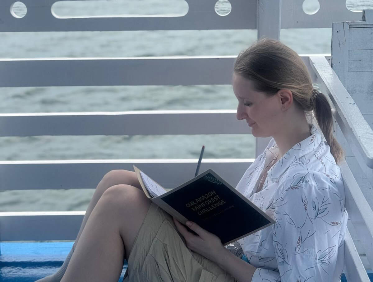 Patricia sitzt auf einem Boot und schreibt in ein Heft zur Amazon Rainforest Challenge