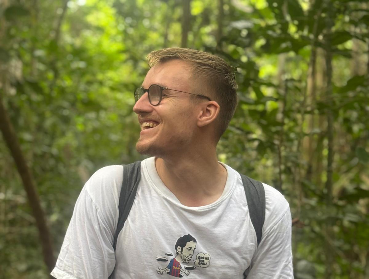 Peter sitzt mit Rucksack auf einem Holzgeländer im Regenwald und blickt zur Seite